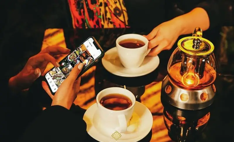 مشتریان در رستوران ایرانی شاندیز ماهان رویال حین نوشیدن چای، منوی غذاهای لذیذ را در گوشی تماشا میکنند.