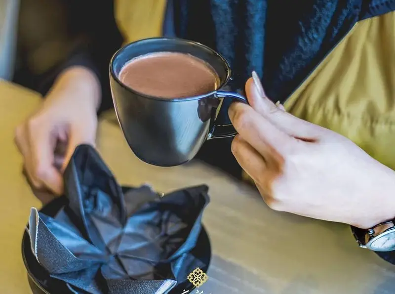 مشتری در رستوران ایرانی شاندیز ماهان رویال در حال لذت بردن از نوشیدنی گرم. تجربه طعم بی‌نظیر قهوه یا هات‌چاکلت در فضایی دلنشین کافه.