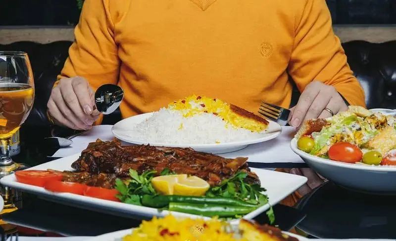 مشتری در حال صرف وعده غذای کامل ایرانی شامل برنج زعفرانی با ته دیگ، خورش و سالاد در رستوران شاندیز ماهان رویال.