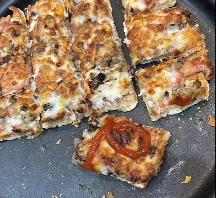 نمایی نزدیک از پیتزای خوشمزه و تازه "فست فود ایرانیان" برش خورده به تکه‌های مربع با پنیر طلایی و سس کچاپ لذیذ.