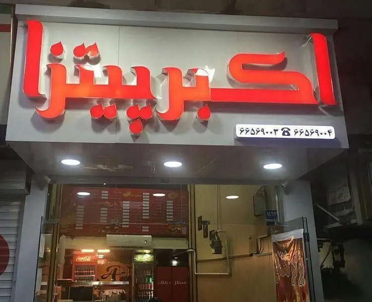 تابلوی سردر فست فود اکبر پیتزا، نمای بیرونی این رستوران با حروف قرمز درخشان و شماره تماس‌های درج شده برای سفارش.