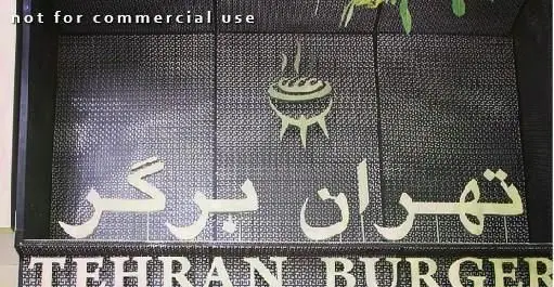 تابلوی کسب و کار "تهران برگر" با نوشته های فارسی و انگلیسی برجسته روی زمینه مشبک تیره، همراه با آیکون کباب پز جهت تبلیغ غذای باکیفیت.