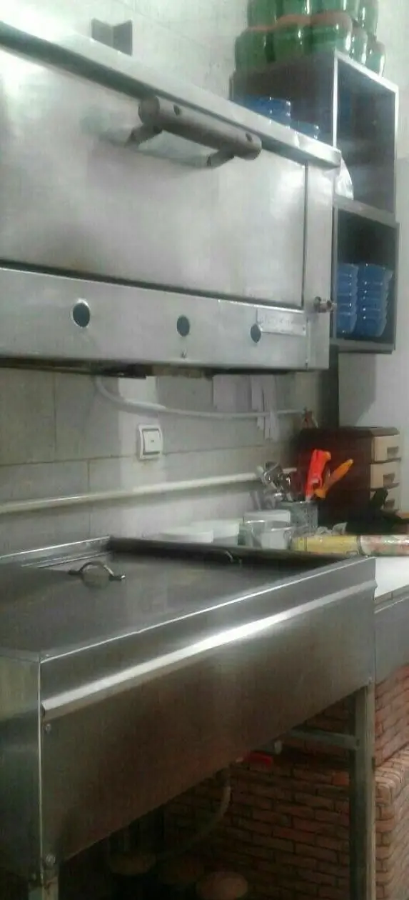 نمای داخلی آشپزخانه صنعتی مدرن رستوران ایرانی دیزی تندوری با میز کار و فر استیل، مجهز برای پخت حرفه‌ای.