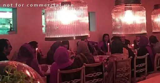 مشتریان در رستوران "غذای سالم و گاهی پیور" از شامی دلنشین لذت می‌برند. فضایی گرم با نورپردازی خاص و جمعی دوستانه.