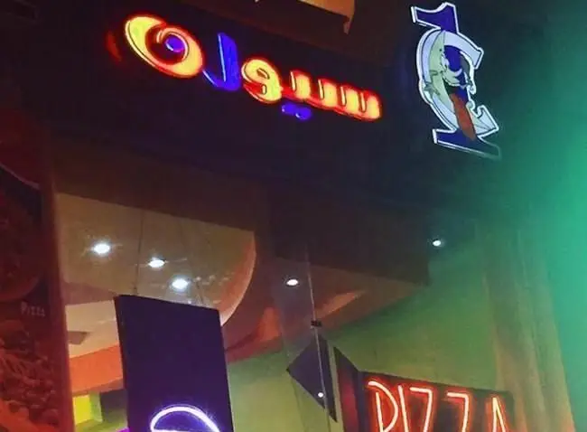 نمای بیرونی کافه و فست فود سیوان با تابلوهای نئونی درخشان شامل نام "سیوان" و لوگوی خاص، به همراه تابلوی "PIZZA" در شب.