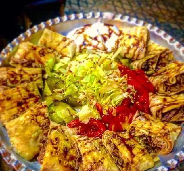 تصویری جذاب از پلاتر کباب ابوعلی: رول‌های کباب پیچیده شده با نان، تزئین شده با سس، به همراه سالاد کاهو، ترشی و سس ماست در دیس بزرگ.