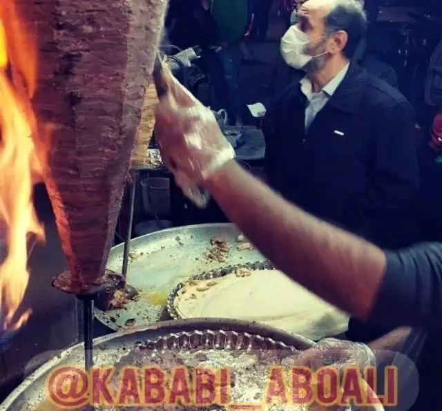 آماده‌سازی لذیذ شاورما در کباب ابوعلی، برش گوشت تازه از سیخ گردان با شعله آتش برای مشتریان مشتاق.