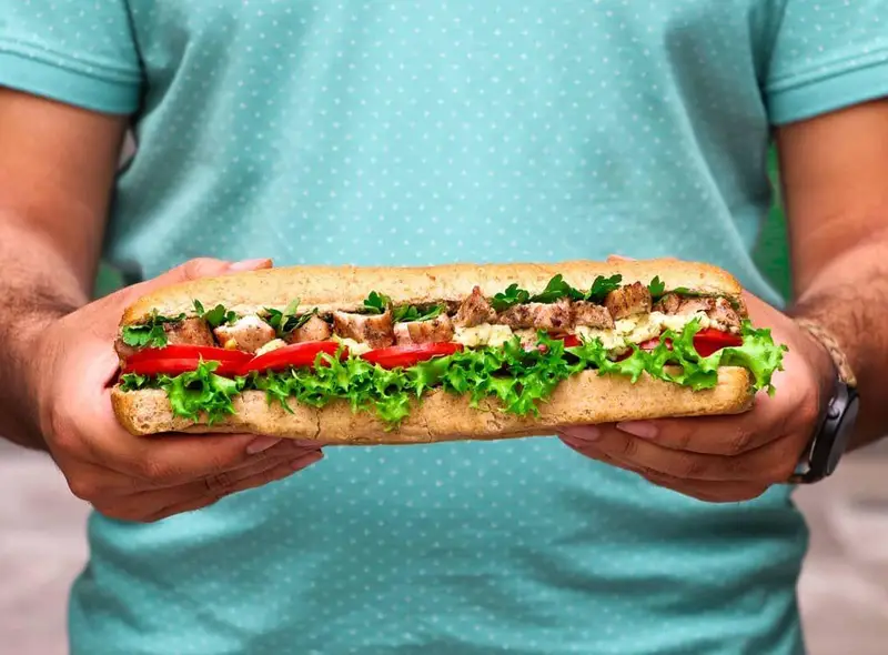 ساندویچ ساب بزرگ با مرغ گریل، کاهو، گوجه و سس در نان سبوس‌دار، از فست فود شیلا. انتخابی سالم و خوشمزه برای وعده شما.