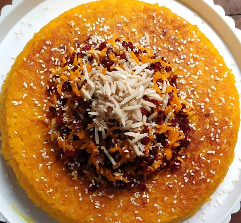 تصویری زیبا از ته چین زعفرانی خوش عطر کترینگ شبگیر، تزئین شده با زرشک، خلال بادام و کنجد، غذای اصیل و مجلسی ایرانی.