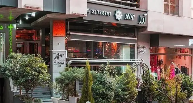 تصویر نمای بیرونی شیک فست فود و پیتزا اوا در خیابان نیاوران تهران، به همراه تابلوی شماره تماس 22728797 و فضای سبز.