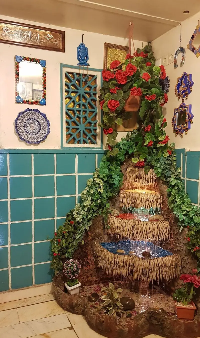 فضای دلنشین و دکوراسیون سنتی دیزی سرای ایرانشهر با آبنمای زیبا، گل و گیاه، مناسب برای تجربه‌ای اصیل از غذای ایرانی.