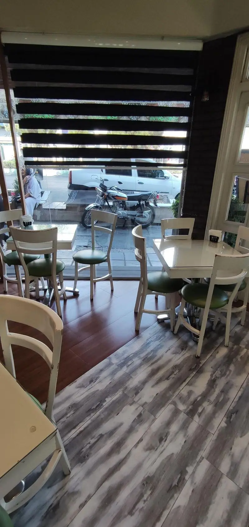 نمای داخلی رستوران ایتالیایی سالی شعبه ستارخان: میز و صندلی‌های شیک، پنجره با پرده کرکره‌ای و منظره خیابان شلوغ شهری.