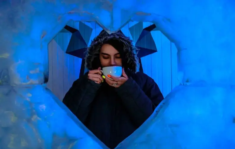 لذت نوشیدن چای گرم در کافه فصل یخ، فضایی جادویی با نورپردازی آبی و قاب قلب یخی. بهترین تجربه در یک کافه یخی منحصر به فرد.