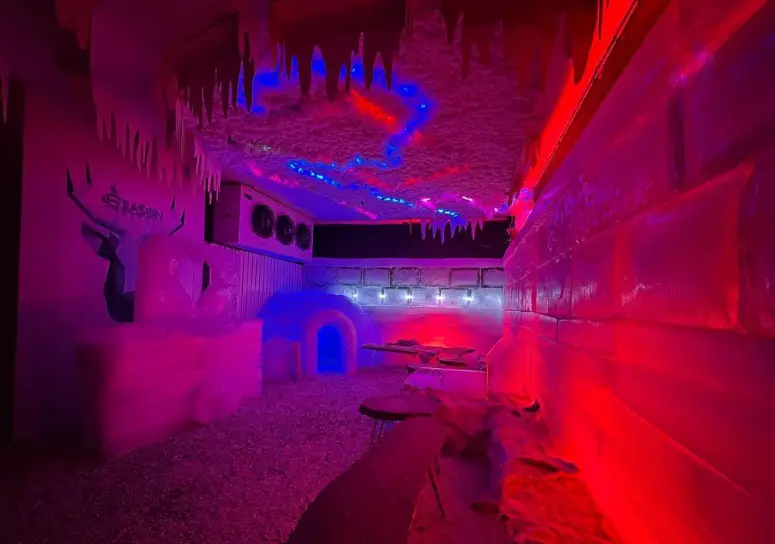 تصویری از کافه یخی فصل یخ با فضایی منحصربه‌فرد، دیوارهای ساخته شده از یخ، سقف پوشیده از قندیل و نورپردازی جذاب.