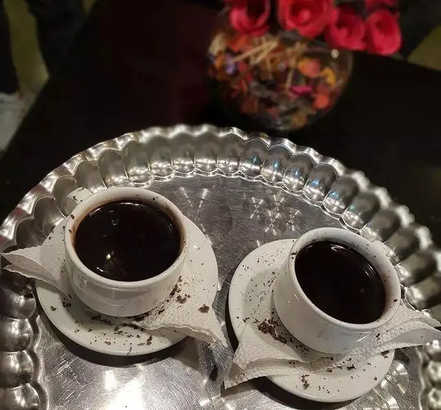 دو فنجان هات چاکلت یا قهوه غلیظ روی سینی نقره ای در محیط دنج کافه و سفره خانه تیام، تجربه ای گرم و به یادماندنی.