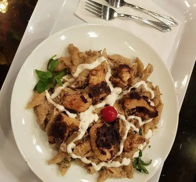 پاستا پنه با تکه‌های مرغ گریل شده، سس سفید خامه‌ای، تزیین شده با سبزی تازه و گیلاس، از منوی کافه و سفره خانه تیام.