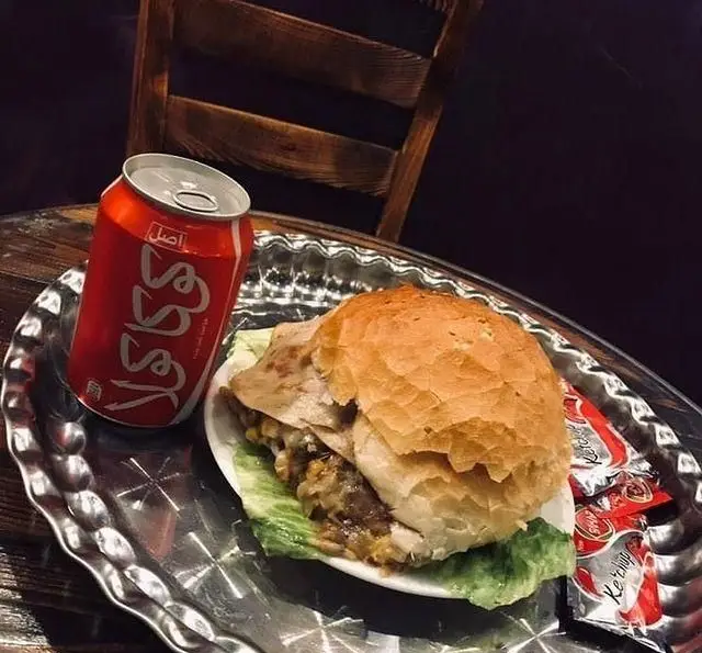 یک برگر لذیذ با نان تازه و نوشابه کوکاکولا در کافه و سفره خانه تیام. غذایی کامل با کاهو و سس کچاپ، سرو شده روی سینی.