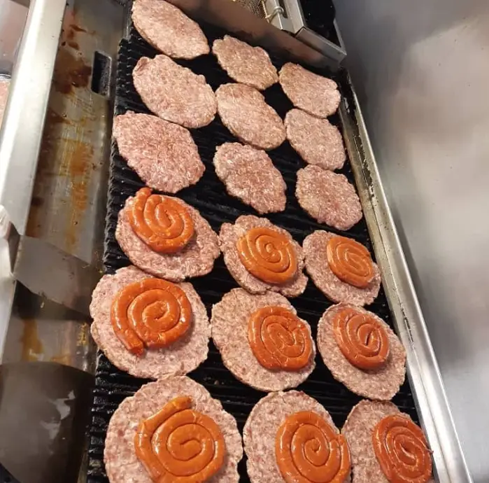 آماده سازی ساندویچ و برگرهای خوشمزه کریم و رحیم: پتی‌های گوشت تازه و سوسیس‌های حلزونی روی گریل آماده پخت.