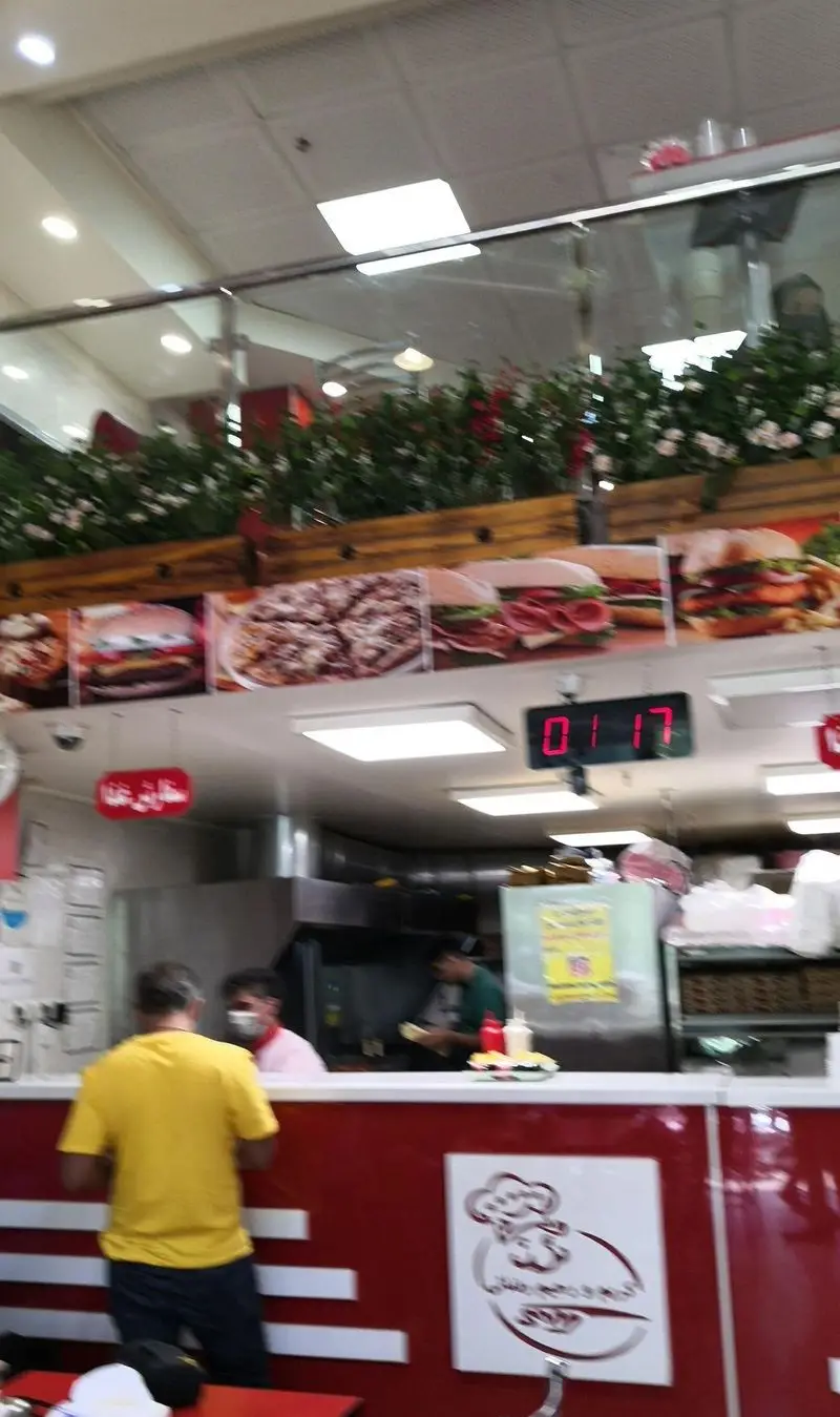 نمای داخلی فست فود ساندویچ و پیتزا کریم و رحیم، شامل منو پیتزا، همبرگر و انواع ساندویچ، مشتری و پرسنل آماده سفارش.