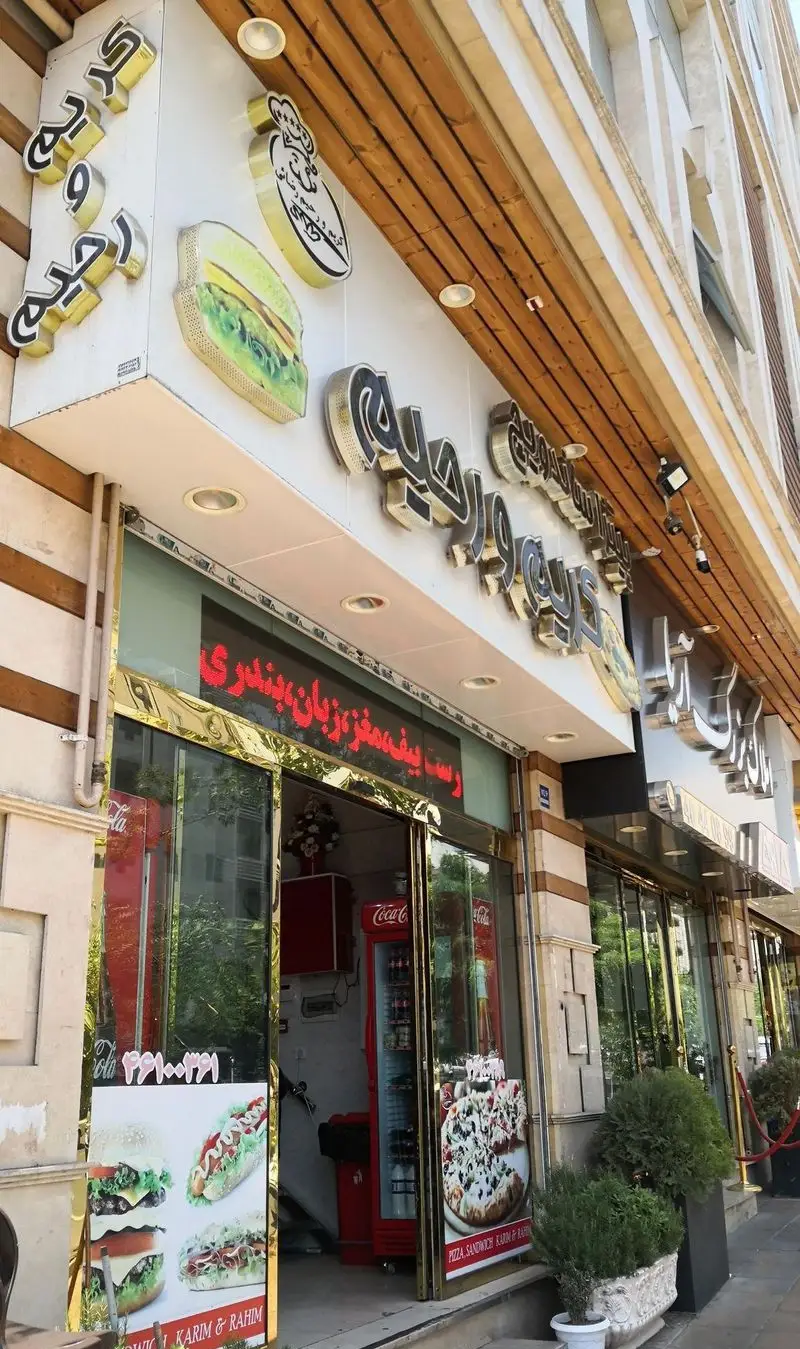 نمای بیرونی ساندویچ و پیتزا کریم و رحیم، با تابلوهای بزرگ و تصاویر برگر، هات داگ، پیتزا، و منوی رست بیف، مغز و زبان، بندری.