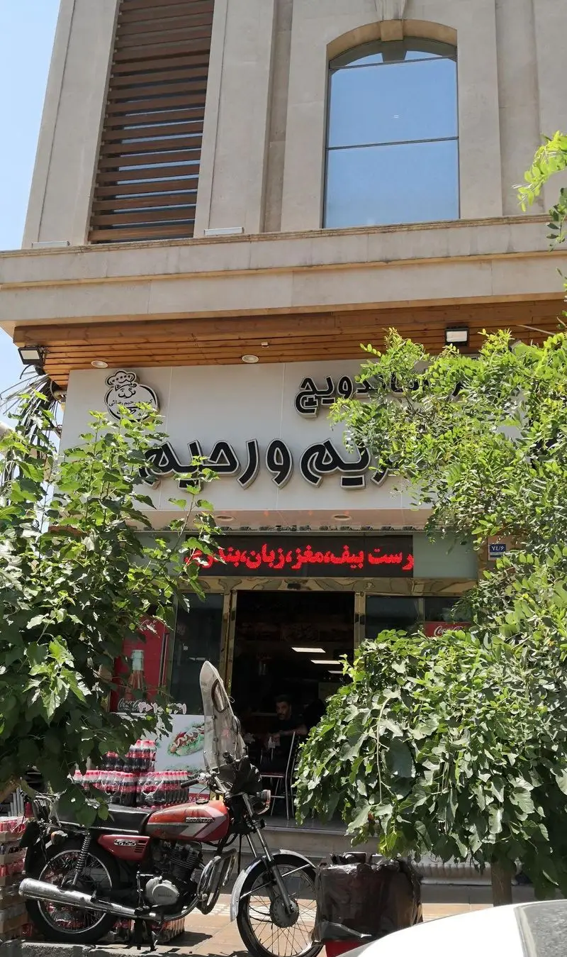 نمای بیرونی مغازه ساندویچ و پیتزا کریم و رحیم، ارائه دهنده رست بیف، مغز، زبان بندری. موتورسیکلت جلوی فست فود.