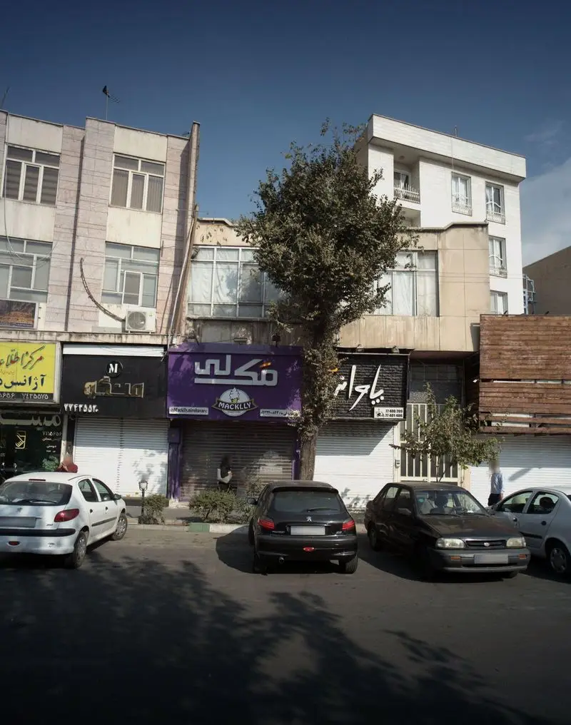 نمای بیرونی مغازه بستنی مکلی نیروهوایی در تهران، با تابلوی بنفش، خودروهای پارک شده و فضای خیابان در یک روز آفتابی.