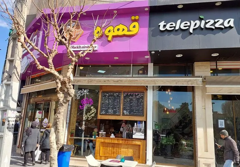 نمای بیرونی کافه جلاتو و وافل مکلی نیروهوایی: سردر بنفش "قهوه"، ورودی چوبی، منو روی تخته سیاه، کنار تله‌پیتزا.