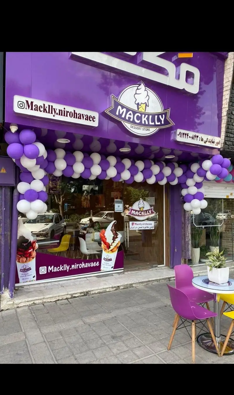 تصویر نمای بیرونی بستنی فروشی و دسر مکلی نیروهوایی با طراحی مدرن و رنگ بنفش. دکوراسیون افتتاحیه با بالن‌های زیبا، میز و صندلی فضای باز برای مشتریان.