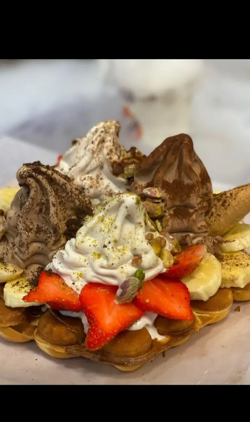 دسر وافل حبابی خوشمزه از بستنی مکلی نیروهوایی: بستنی سافت سرو شکلاتی و وانیلی، توت فرنگی تازه، موز، پسته و پودر کاکائو.