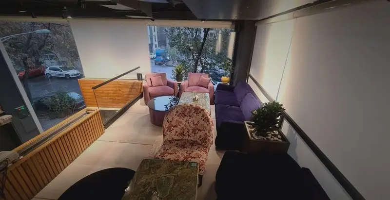 فضای داخلی دنج کافه رستوران صدصا، شامل مبلمان راحتی صورتی و بنفش، میزهای شیشه‌ای و چوبی، با پنجره‌هایی رو به منظره شهری شلوغ