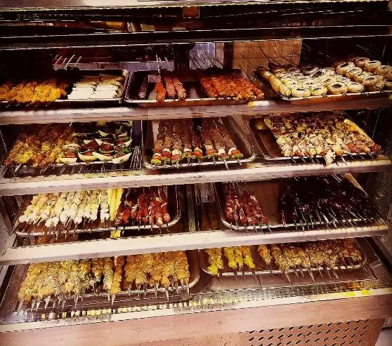 عمو امید: ویترین بزرگ و جذاب کباب‌های متنوع از جوجه، گوشت، سبزیجات و کباب کوبیده تازه، آماده سرو در رستوران.