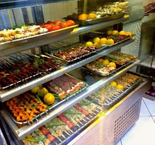 ویترین جذاب کباب‌سرای عمو امید؛ شامل انواع کباب‌های سیخی تازه گوشت، جوجه، میگو و سبزیجات آماده گریل و طبخ.