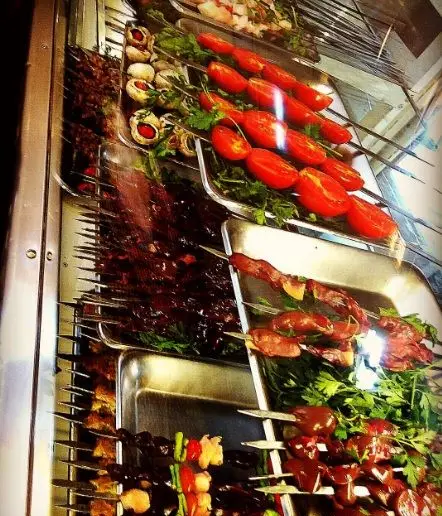 کباب‌های تازه و خوش‌رنگ شامل جگر، گوشت، گوجه و قارچ روی سیخ، آماده برای مشتریان عمو امید، نمایشگاهی از غذای ایرانی سنتی.