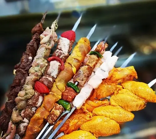 مجموعه‌ای از سیخ‌های کباب تازه و متنوع عمو امید: کباب گوشت، جوجه کباب زعفرانی، کباب چنجه، و بال مرغ آماده برای طبخ و پذیرایی.