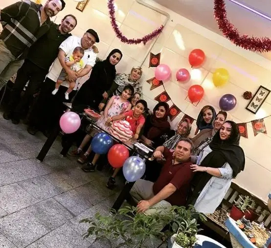 دورهمی شاد و صمیمی جشن تولد در فضای کسب و کار عمو امید، با کیک سه طبقه، بادکنک‌های رنگی و جمعی از مهمانان.
