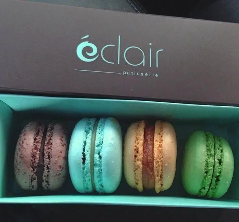 چهار ماکارون زیبا و خوشمزه از شیرینی اکلر در جعبه‌ای شیک، با طعم‌های متنوع قهوه‌ای، آبی، کرم و سبز، مناسب برای لحظات شیرین.