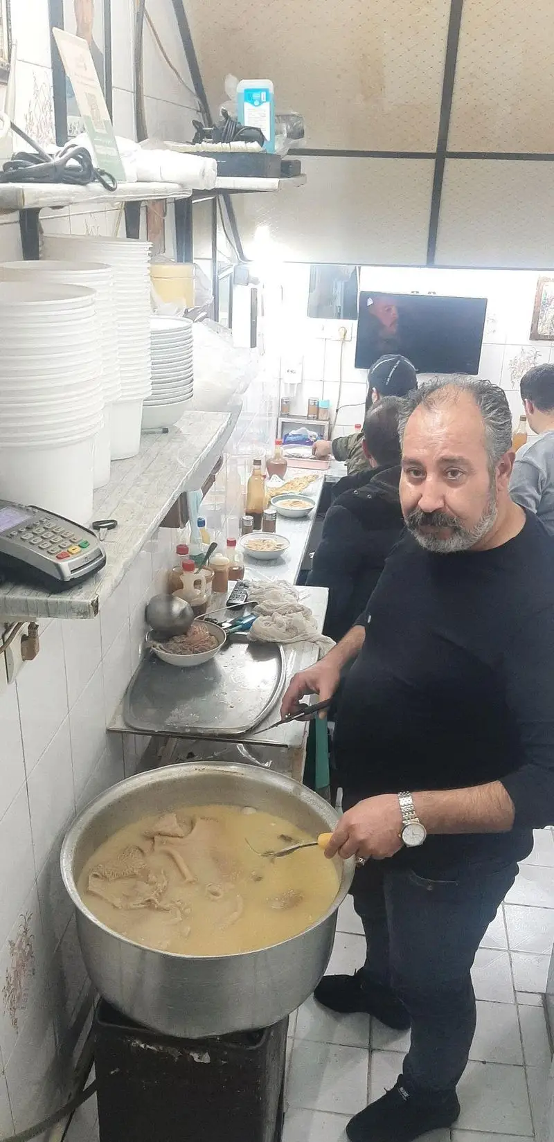 سرآشپز طباخی منوچهر در حال طبخ کله پاچه لذیذ در قابلمه بزرگ برای مشتریان. آماده‌سازی غذای سنتی ایرانی در فضای رستوران.