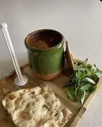 مستر دیزی: تصویری دلپذیر از یک کاسه دیزی یا آبگوشت سنتی ایرانی داغ، همراه با نان تازه و سبزی خوردن معطر روی سینی چوبی.