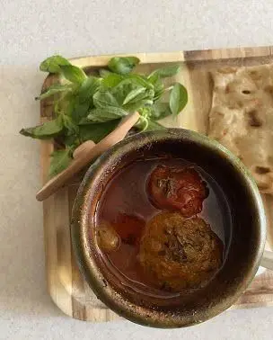 کاسه دیزی سنتی مستر دیزی با آبگوشت غلیظ، گوشت کوب، نان تازه و سبزی ریحان معطر برای تجربه یک غذای ایرانی اصیل.