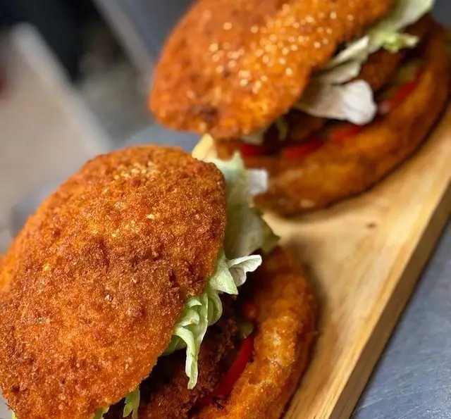 دو ساندویچ سوخاری طلایی و خوشمزه از پیتزا چوکوتا، حاوی مرغ و کاهو، روی تخته سرو چوبی برای سفارش آماده‌اند.