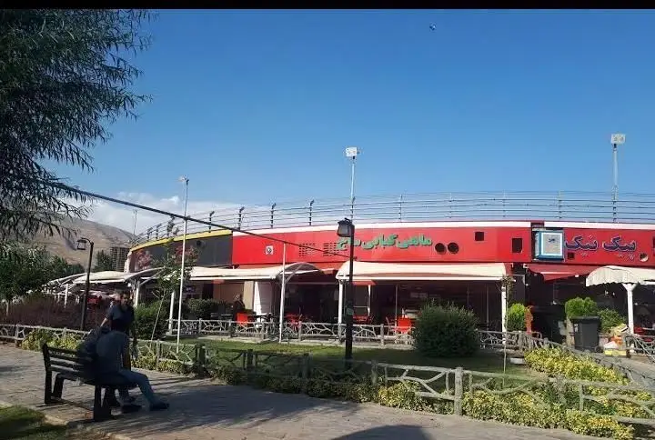 تصویر بیرونی شعبه عطاویچ با ساختمان قرمز رنگ و سقف سفید، دارای محوطه فضای باز، میز و صندلی برای مشتریان در روزی آفتابی.