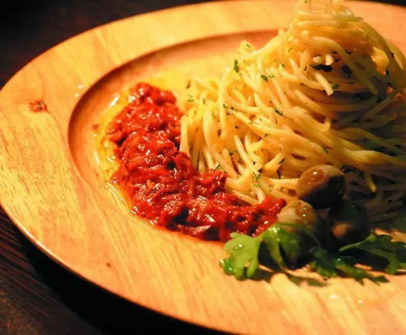 پاستا اسپاگتی خوشمزه و تازه با سس قرمز و زیتون در بشقاب چوبی، آماده سرو در فست فود دالون، تجربه‌ای لذیذ از غذای ایتالیایی.