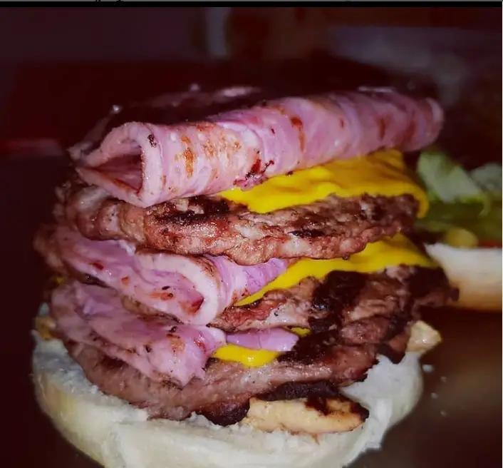 تصویری از یک همبرگر غول‌پیکر و چندلایه از پیتزا و ساندویچ سبحانی، شامل چندین لایه گوشت گریل‌شده، پنیر چدار آب‌شده و ژامبون/بیکن.