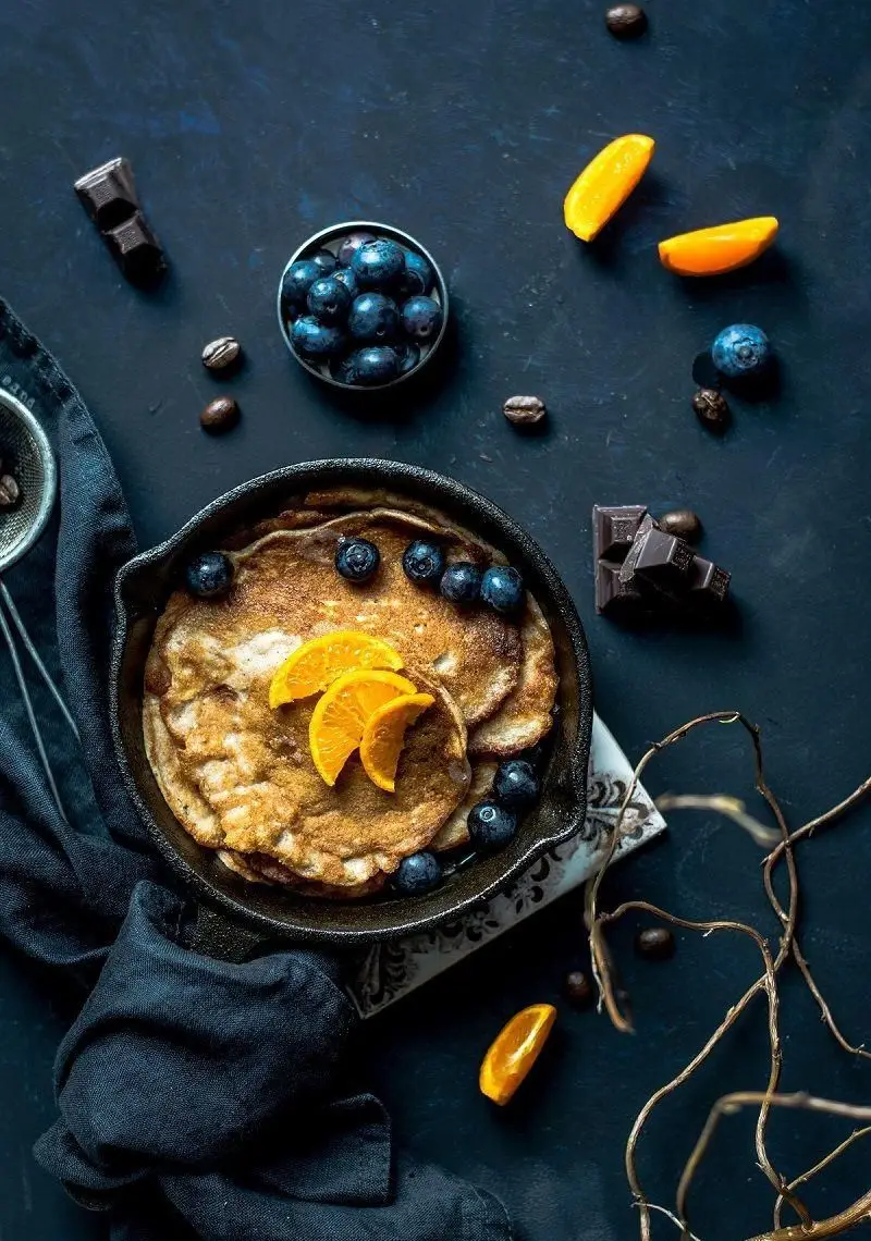 صبحانه دلپذیر: پنکیک‌های طلایی با بلوبری و پرتقال تازه. دانه قهوه و شکلات تلخ. خدمات غذایی کترینگ صنعتی طعام یاس.