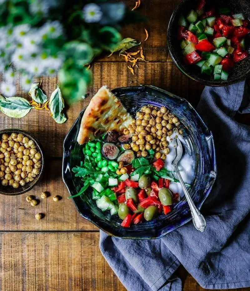 منوی سالم و متنوع کترینگ صنعتی طعام یاس: کاسه غذای مدیترانه‌ای با نخود، سبزیجات تازه، زیتون، انجیر و نان. مناسب غذای شرکتی.