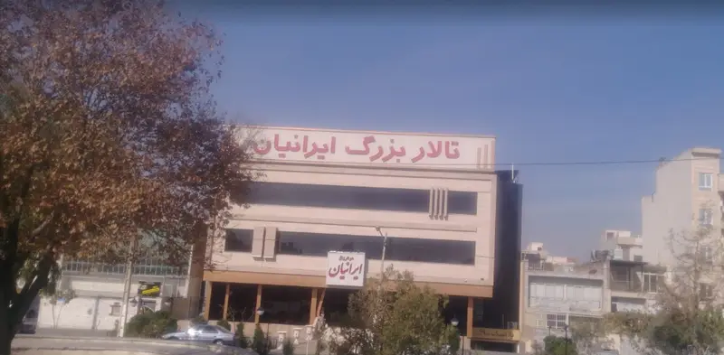 تصویری با کیفیت از نمای ساختمان تالار بزرگ ایرانیان، مکانی مجلل برای برگزاری جشن‌ها، عروسی‌ها و مراسم خاص، با آسمانی آبی و درختان در اطراف.