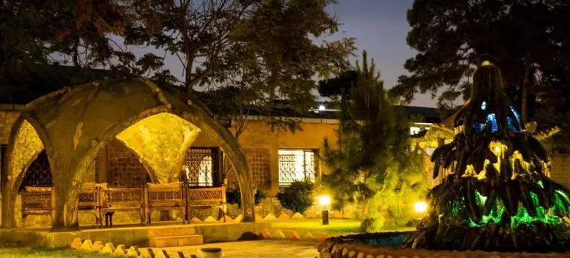 رستوران سنتی سپیدار در شب: آلاچیق سنتی با نورپردازی گرم، نیمکت‌های چوبی، ساختمان و آبنمای رنگی؛ محیطی دلنشین.