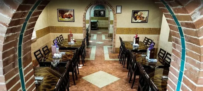 نمای دلنشین و سنتی رستوران سپیدار با طاق‌های آجری و کاشی‌کاری آبی، میز و صندلی‌های چوبی آماده پذیرایی مهمانان در فضایی آرام.