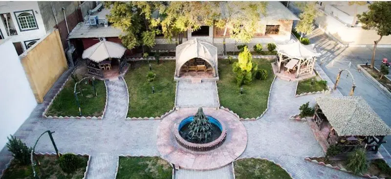 نمای هوایی از محیط زیبای رستوران سنتی سپیدار با آلاچیق‌های چوبی، حوض و فواره مرکزی و فضای سبز دلنشین برای صرف غذا.