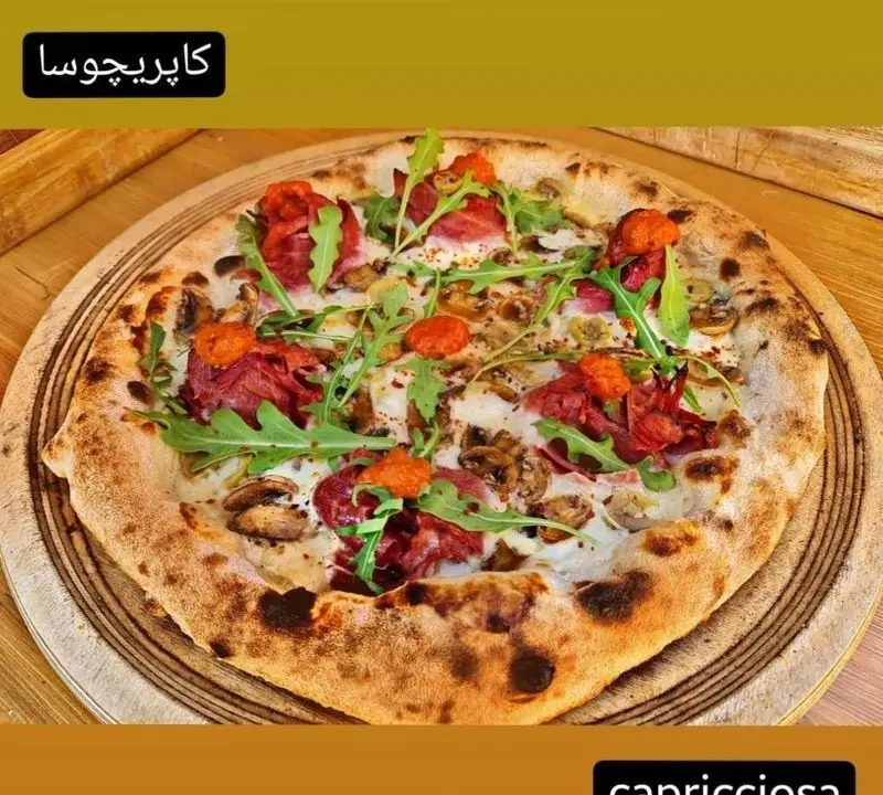 تصویری از پیتزا کاپریچوسا ایتالیایی و لذیذ "کوچینا پیتزا" با نان برشته، قارچ، روکولا و ژامبون ممتاز، آماده سرو داغ.